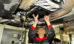 Mechanik pod samochodem wykonuje wymianę oleju w skrzyni biegów, czy to dynamiczna czy statyczna, z użyciem węży i specjalistycznego sprzętu.