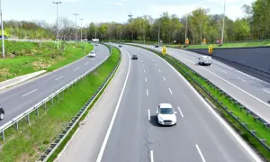 Autostrada z zielonymi pasami i drzewami. Samochody jadą z różną prędkością, przypominając o minimalnej prędkości na autostradzie.