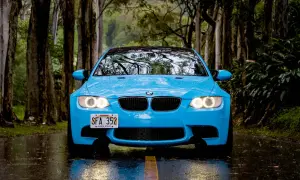 Niebieskie BMW na mokrej drodze, wśród drzew. Świetna przyczepność na mokrej nawierzchni zapewnia bezpieczeństwo podczas jazdy w deszczu.