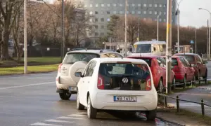Biały Volkswagen up! i inne samochody stoją na pasach dla pieszych, blokując skrzyżowanie.
