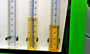 Trzy menzurki z podziałką. W dwóch z nich widać żółtawy płyn, prawdopodobnie paliwo w oleju, na poziomie około 50 i 40 ml.