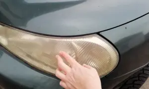 Dłoń pokazuje zażółconą lampę samochodową, sugerując czyszczenie lamp samochodowych WD-40.