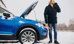 Mężczyzna z telefonem i szczotką przy niebieskim samochodzie z otwartą maską na śniegu. Czy można jechać bez płynu chłodniczego?