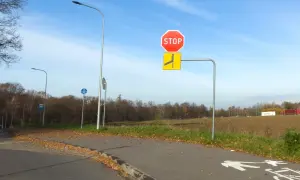 Znak STOP i znak informujący o łamanym pierwszeństwie po lewej stronie drogi. Jesień, liście na ścieżce rowerowej.