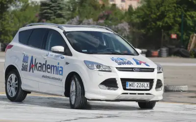 Biały Ford Kuga z napisem "Auto Świat Akademia" na drzwiach, idealny do nauki techniki jazdy samochodem dla początkujących.