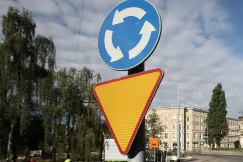 Rondo bez znaku ustąp pierwszeństwa. Znak informuje o ruchu okrężnym, a obok niego znajduje się żółty trójkątny znak ostrzegawczy.