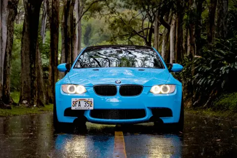 Niebieskie BMW na mokrej drodze, wśród drzew. Świetna przyczepność na mokrej nawierzchni zapewnia bezpieczeństwo podczas jazdy w deszczu.