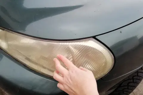 Dłoń pokazuje zażółconą lampę samochodową, sugerując czyszczenie lamp samochodowych WD-40.
