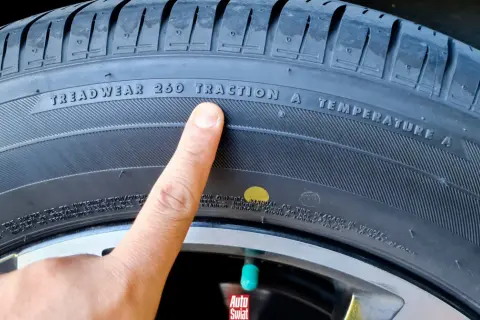 Palec wskazuje na oznaczenie TREADWEAR 260 TRACTION A TEMPERATURE A na oponie. Obok widoczna jest żółta kropka.