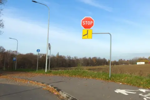 Znak STOP i znak informujący o łamanym pierwszeństwie po lewej stronie drogi. Jesień, liście na ścieżce rowerowej.