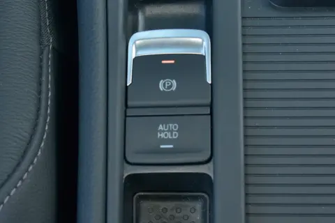 Przycisk "AUTO HOLD" w samochodzie, obok hamulca ręcznego. Ułatwia postój bez trzymania pedału hamulca.
