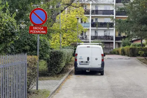 Znak "zakaz zatrzymywania się" i "droga pożarowa" ostrzega przed konsekwencjami, jaki mandat za parkowanie na zakazie grozi kierowcy białego vana.