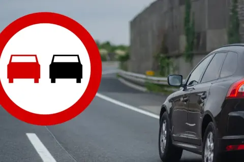 Znak zakazu wyprzedzania. Czerwony okrąg z dwoma samochodami, jeden czerwony, drugi czarny. Na drodze czarny SUV.
