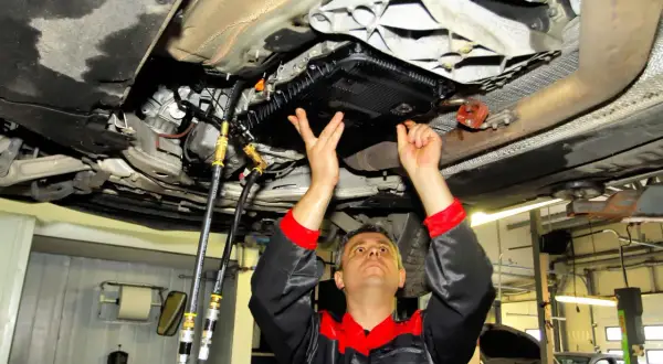 Mechanik pod samochodem wykonuje wymianę oleju w skrzyni biegów, czy to dynamiczna czy statyczna, z użyciem węży i specjalistycznego sprzętu.