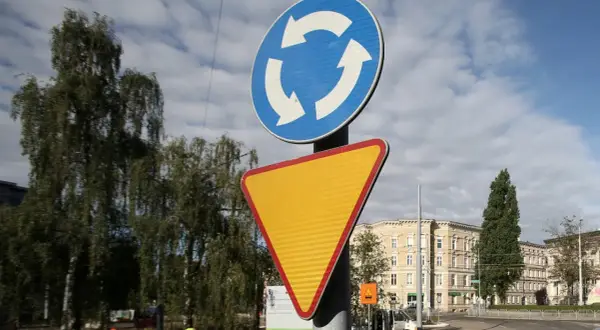 Rondo bez znaku ustąp pierwszeństwa. Znak informuje o ruchu okrężnym, a obok niego znajduje się żółty trójkątny znak ostrzegawczy.