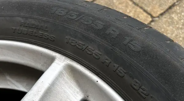 Opona samochodowa 185/55 R 15, widoczna na zewnątrz, na tle kostki brukowej.