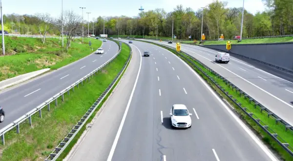 Autostrada z zielonymi pasami i drzewami. Samochody jadą z różną prędkością, przypominając o minimalnej prędkości na autostradzie.