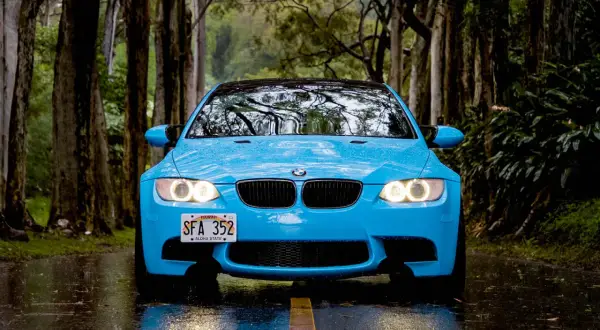 Niebieskie BMW na mokrej drodze, wśród drzew. Świetna przyczepność na mokrej nawierzchni zapewnia bezpieczeństwo podczas jazdy w deszczu.