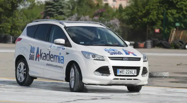 Biały Ford Kuga z napisem "Auto Świat Akademia" na drzwiach, idealny do nauki techniki jazdy samochodem dla początkujących.