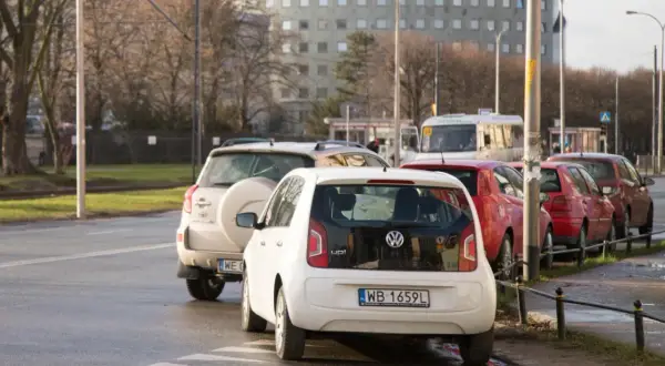 Biały Volkswagen up! i inne samochody stoją na pasach dla pieszych, blokując skrzyżowanie.