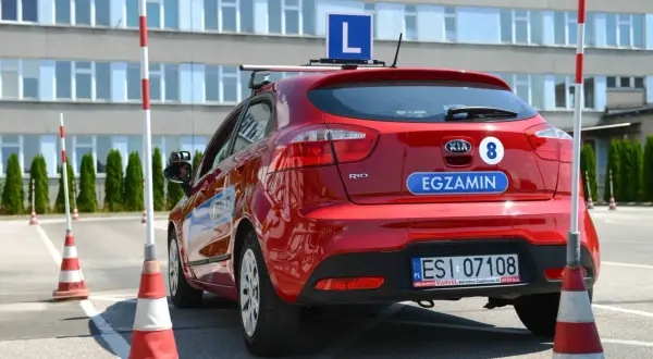 Czerwony samochód z literą "L" na dachu i napisem "EGZAMIN" na klapie bagażnika, gotowy do nauki, jak zdać to cholerne prawo jazdy.