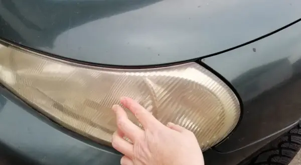 Dłoń pokazuje zażółconą lampę samochodową, sugerując czyszczenie lamp samochodowych WD-40.