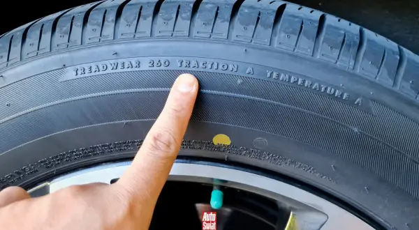 Palec wskazuje na oznaczenie TREADWEAR 260 TRACTION A TEMPERATURE A na oponie. Obok widoczna jest żółta kropka.