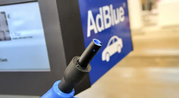 Niebieski pistolet do tankowania AdBlue na stacji paliw. Obok ekran z ceną i logo AdBlue z samochodem. Nie jest to benzyna.