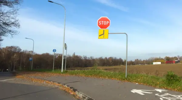 Znak STOP i znak informujący o łamanym pierwszeństwie po lewej stronie drogi. Jesień, liście na ścieżce rowerowej.