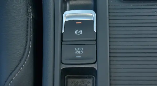 Przycisk "AUTO HOLD" w samochodzie, obok hamulca ręcznego. Ułatwia postój bez trzymania pedału hamulca.