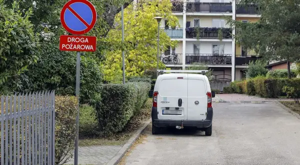 Znak "zakaz zatrzymywania się" i "droga pożarowa" ostrzega przed konsekwencjami, jaki mandat za parkowanie na zakazie grozi kierowcy białego vana.