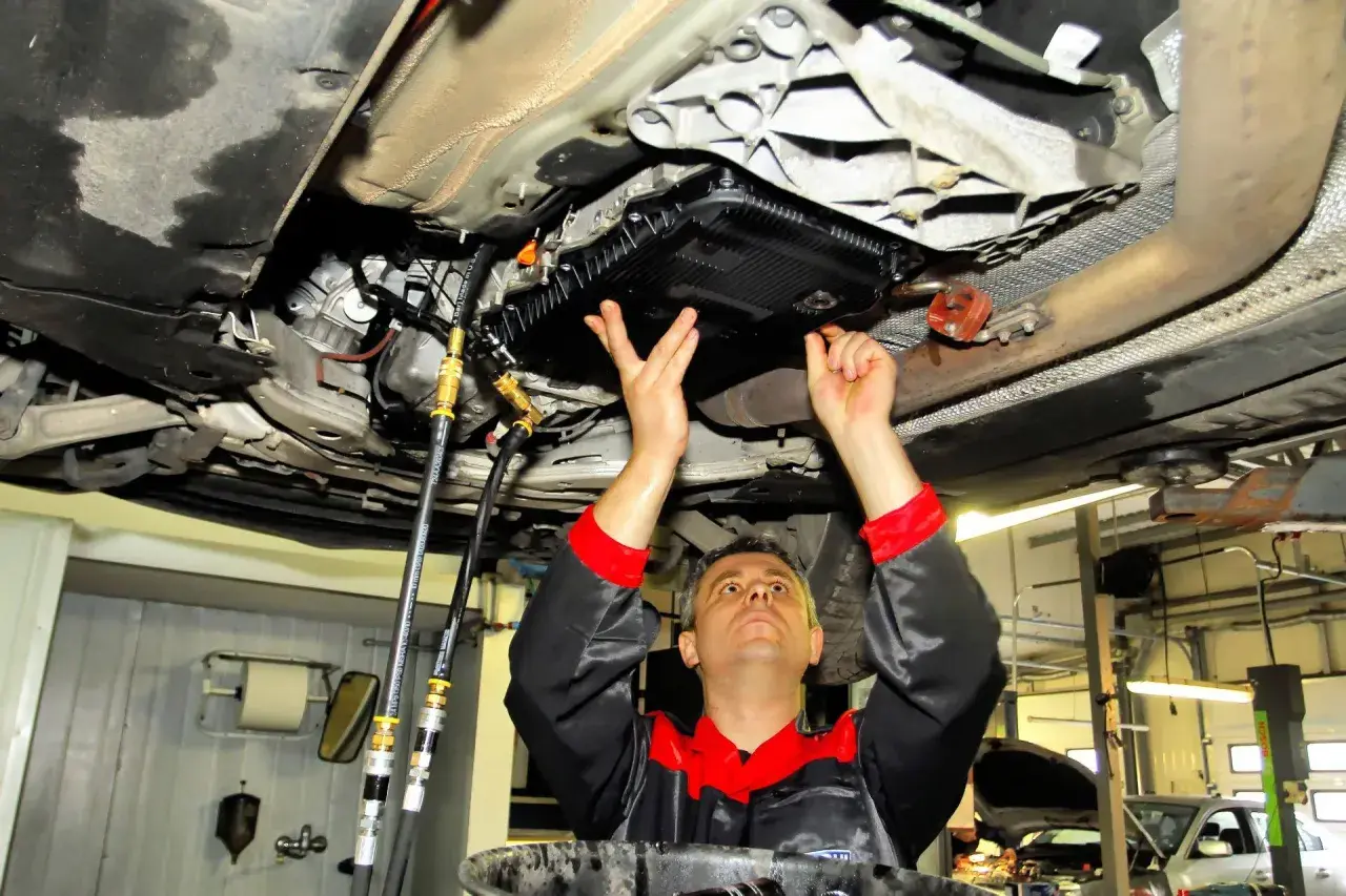 Mechanik pod samochodem wykonuje wymianę oleju w skrzyni biegów, czy to dynamiczna czy statyczna, z użyciem węży i specjalistycznego sprzętu.