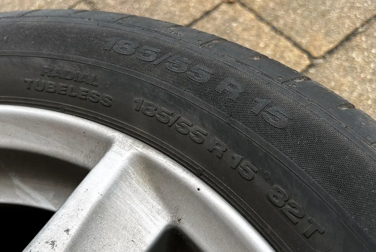 Opona samochodowa 185/55 R 15, widoczna na zewnątrz, na tle kostki brukowej.