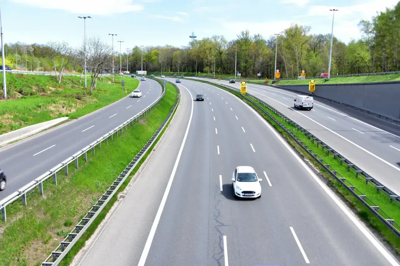 Autostrada z zielonymi pasami i drzewami. Samochody jadą z różną prędkością, przypominając o minimalnej prędkości na autostradzie.