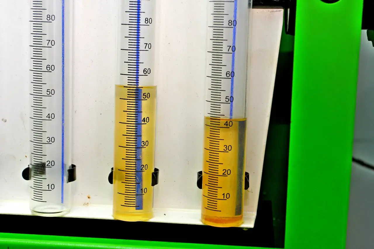 Trzy menzurki z podziałką. W dwóch z nich widać żółtawy płyn, prawdopodobnie paliwo w oleju, na poziomie około 50 i 40 ml.