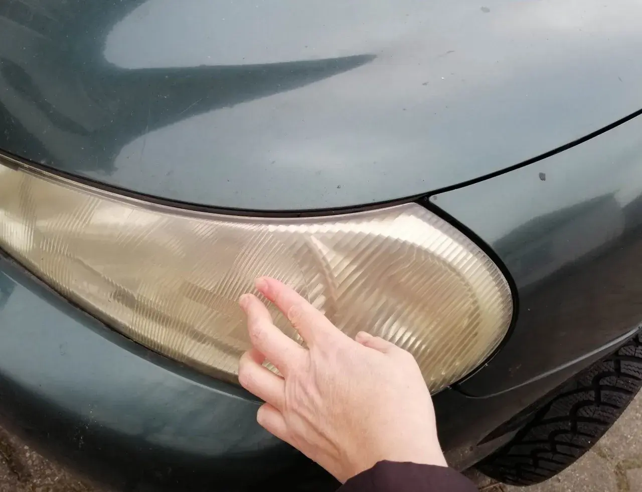 Dłoń pokazuje zażółconą lampę samochodową, sugerując czyszczenie lamp samochodowych WD-40.