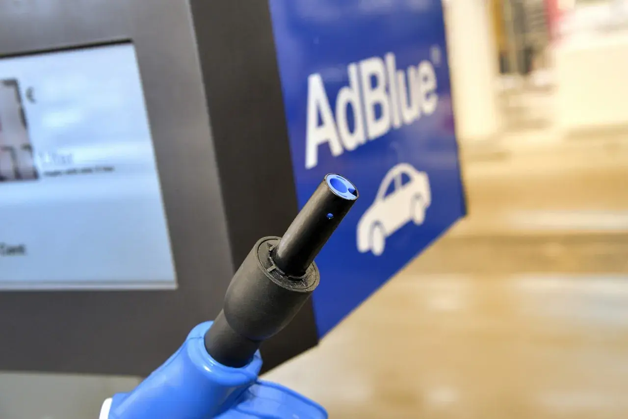 Niebieski pistolet do tankowania AdBlue na stacji paliw. Obok ekran z ceną i logo AdBlue z samochodem. Nie jest to benzyna.
