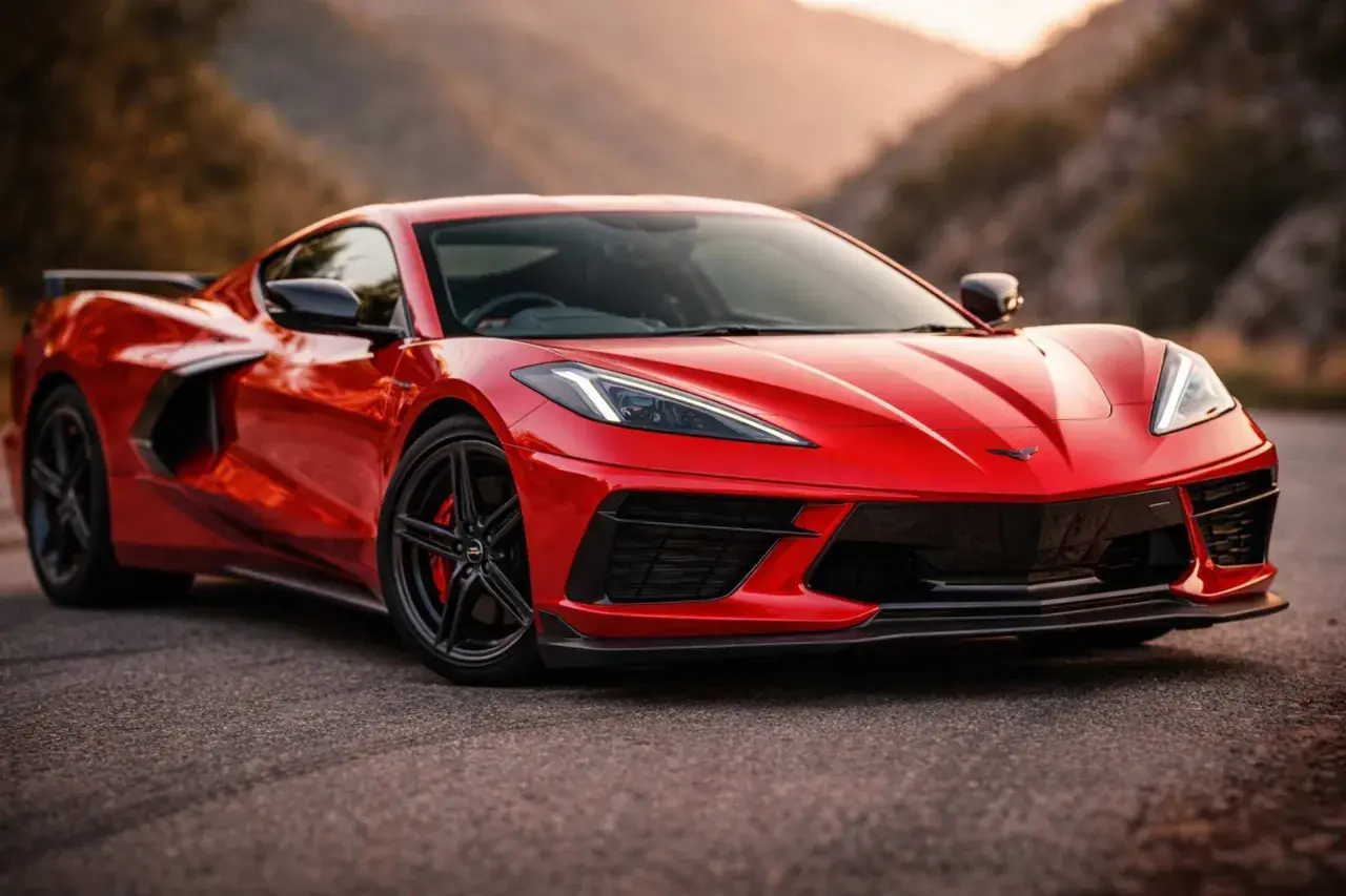 Czerwony Chevrolet Corvette C8 z czarnymi felgami i ostrymi światłami, które przypominają czerwone kierunkowskazy, na tle górskiego krajobrazu.