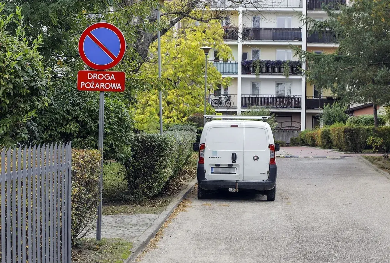 Znak "zakaz zatrzymywania się" i "droga pożarowa" ostrzega przed konsekwencjami, jaki mandat za parkowanie na zakazie grozi kierowcy białego vana.