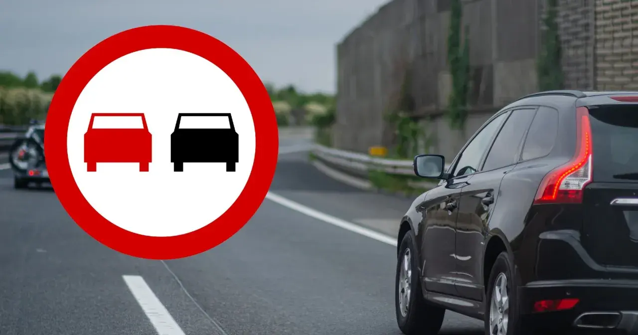 Znak zakazu wyprzedzania. Czerwony okrąg z dwoma samochodami, jeden czerwony, drugi czarny. Na drodze czarny SUV.