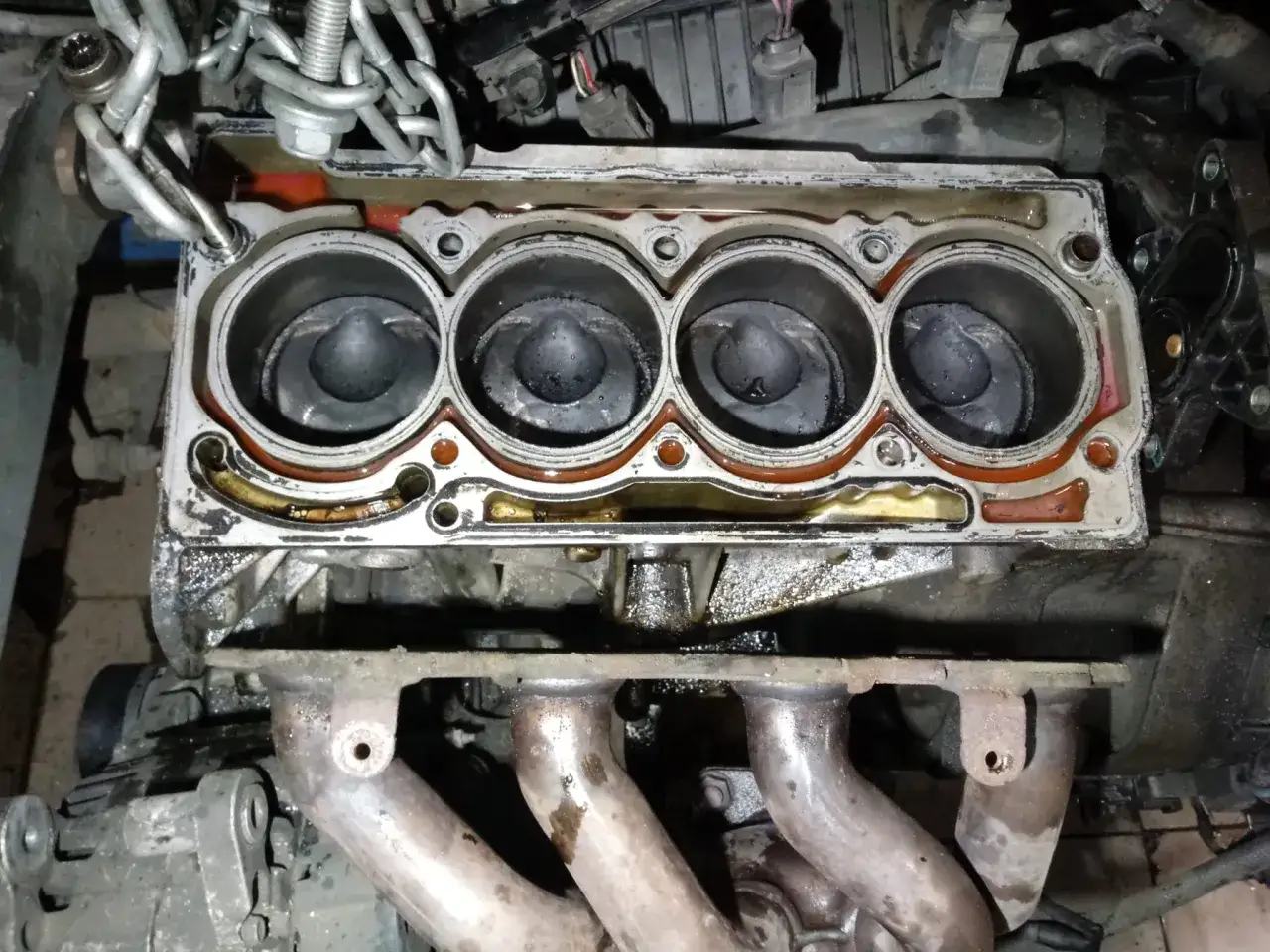 Widok na cztery cylindry silnika z widocznymi śladami oleju i uszkodzeń. Wygląda na to, że doszło do wydmuchanej uszczelki pod głowicą.