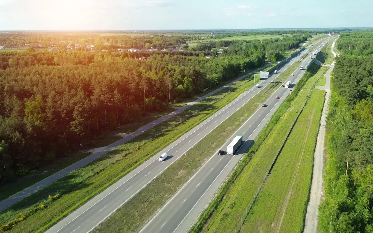 Słońce nad lasem i autostradą. Czy na autostradzie można wyprzedzać z prawej strony? Ruch samochodów i ciężarówek na wielopasmowej drodze.