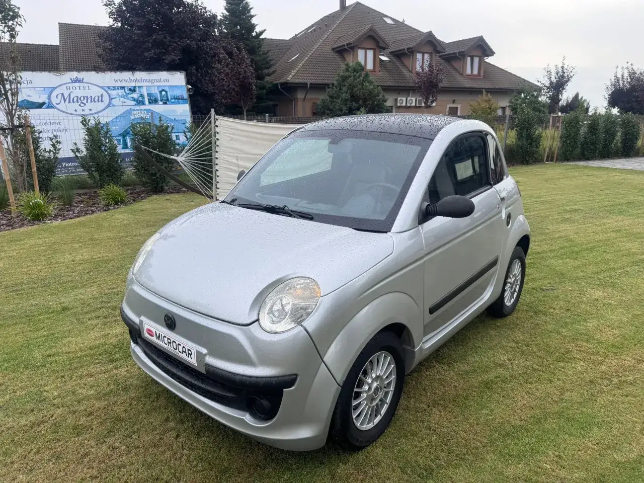 Srebrny microcar na trawniku, idealny do nauki jazdy z prawem jazdy AM.