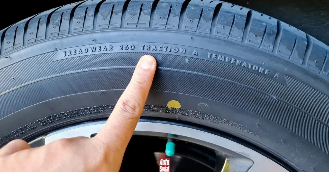 Palec wskazuje na oznaczenie TREADWEAR 260 TRACTION A TEMPERATURE A na oponie. Obok widoczna jest ż&oacute;łta kropka.