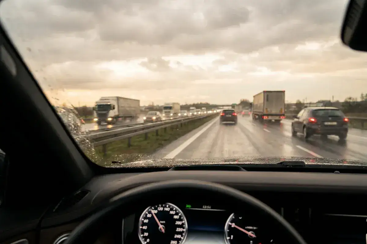 Widok z kabiny samochodu na mokrą autostradę. Samochody i ciężarówki jadą w deszczu, zbliżając się do minimalnej prędkości na autostradzie.