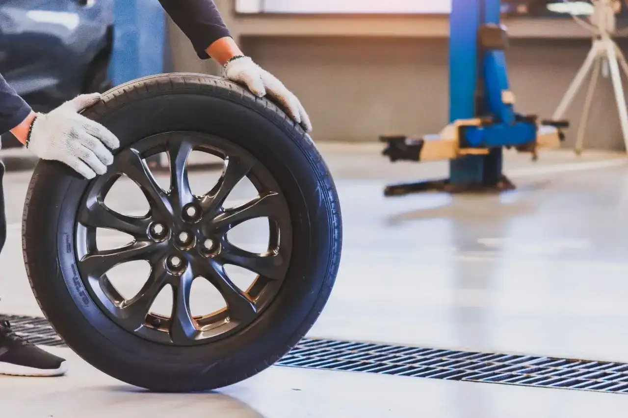 Mechanik w białych rękawiczkach trzyma koło. Niewyważone koła objawy mogą prowadzić do wibracji i nierównomiernego zużycia opon.