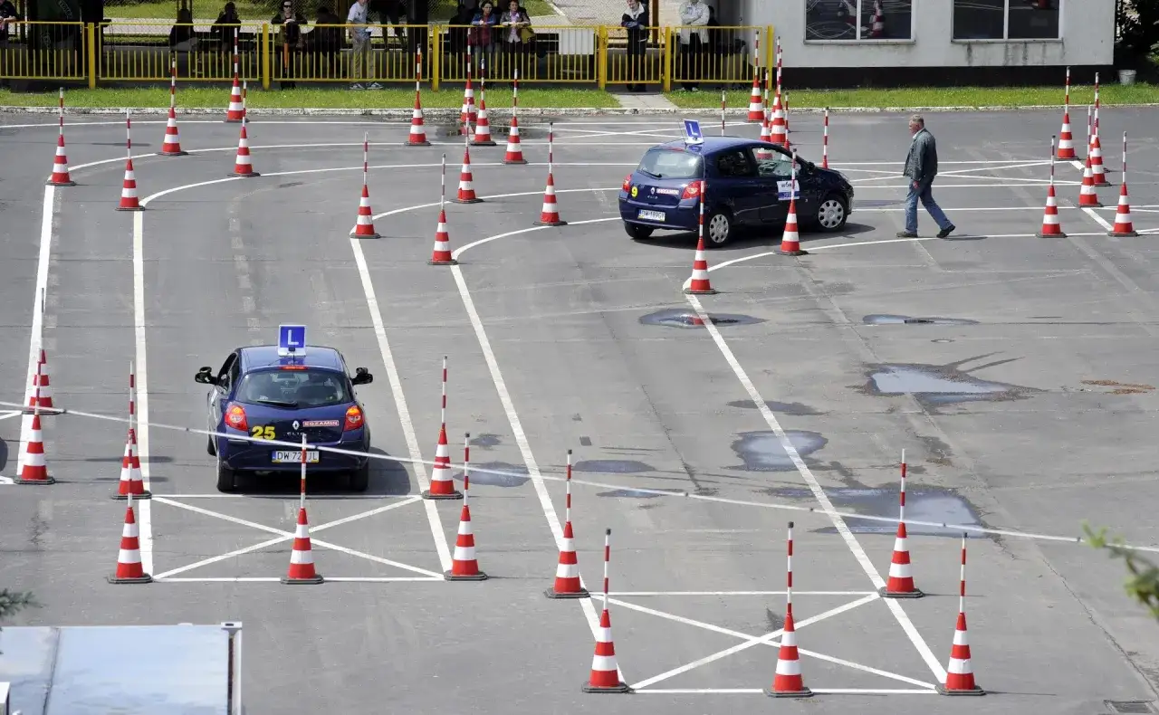 Tor przeszk&oacute;d na placu manewrowym, gdzie kursanci uczą się, jak zdać to cholerne prawo jazdy. Dwa niebieskie samochody z literą 