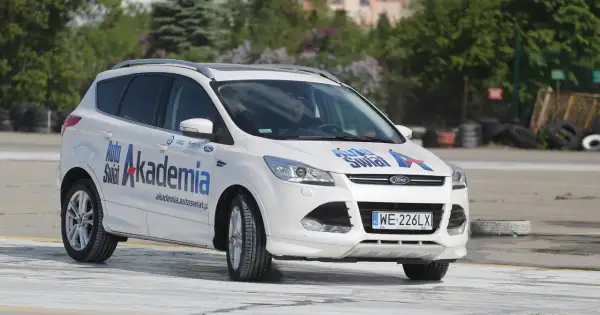 Biały Ford Kuga z napisem "Auto Świat Akademia" na drzwiach, idealny do nauki techniki jazdy samochodem dla początkujących.
