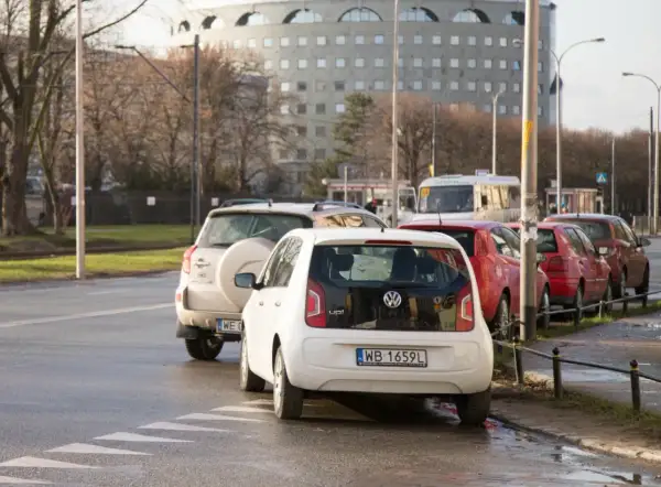 Biały Volkswagen up! i inne samochody stoją na pasach dla pieszych, blokując skrzyżowanie.