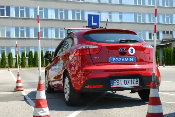 Czerwony samochód z literą "L" na dachu i napisem "EGZAMIN" na klapie bagażnika, gotowy do nauki, jak zdać to cholerne prawo jazdy.